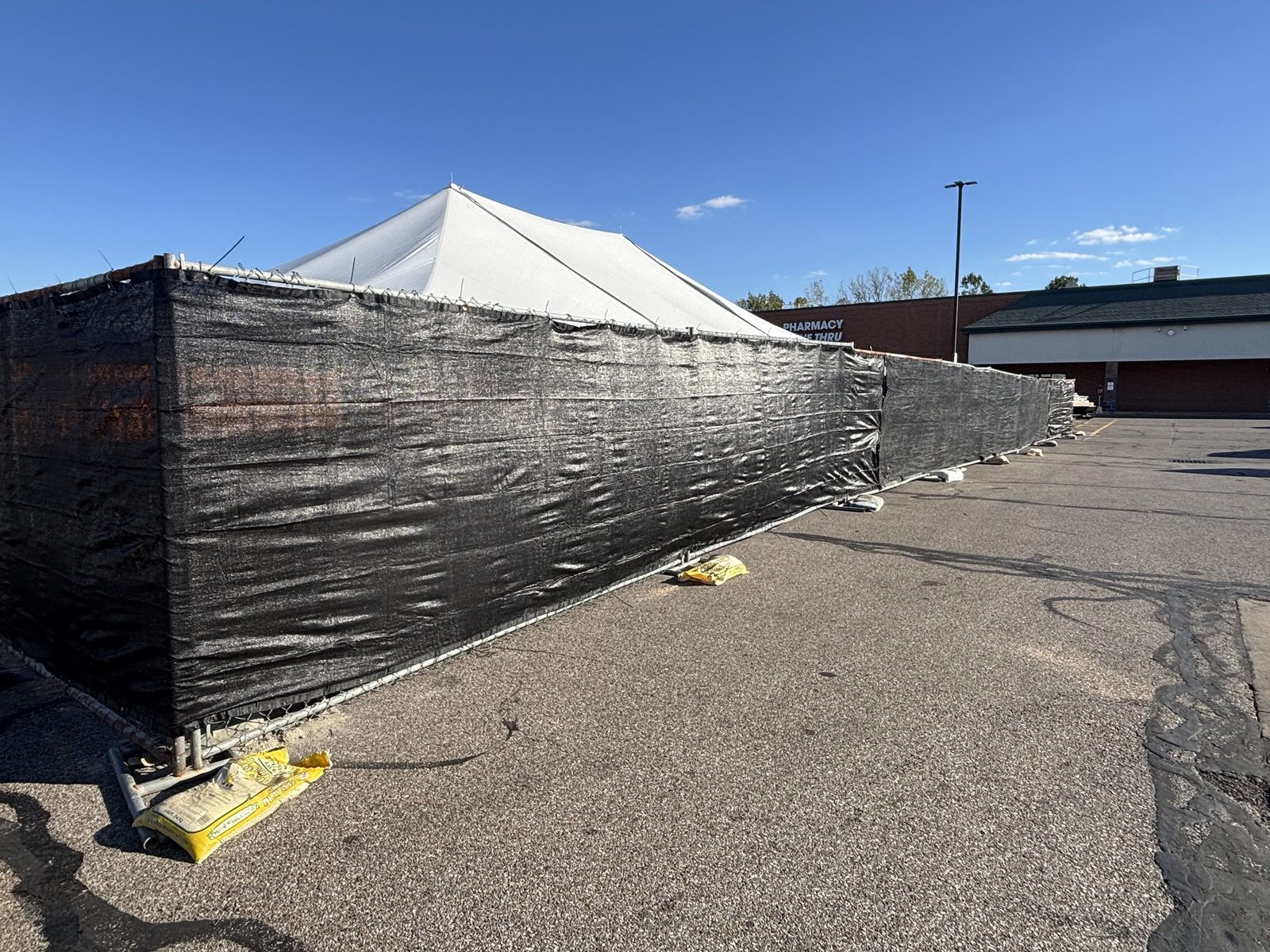 Black windscreen on a panel fence around a white event tent in a parking lot