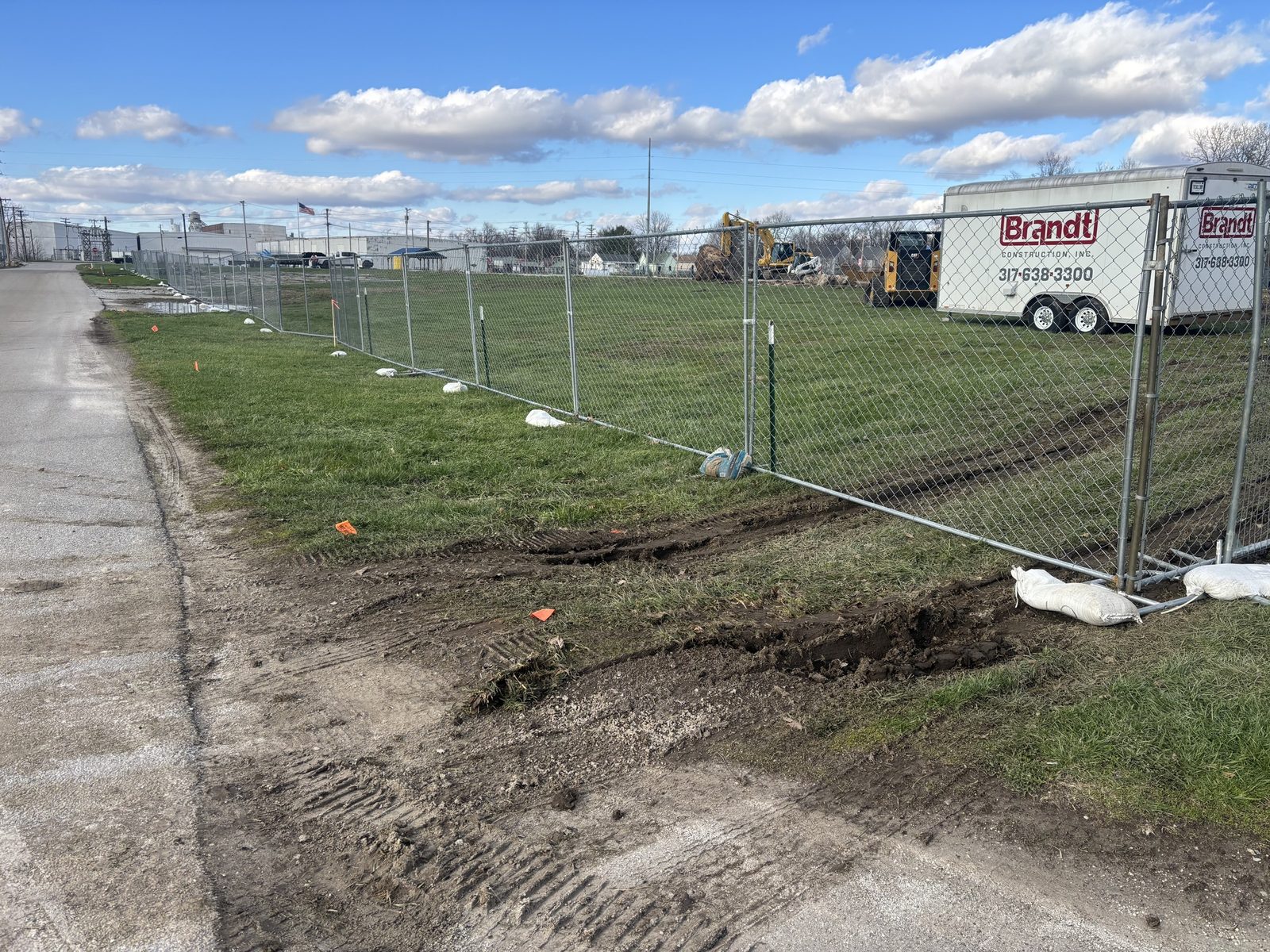 Panel fence on sandbags along a muddy site edge with equipment beyond