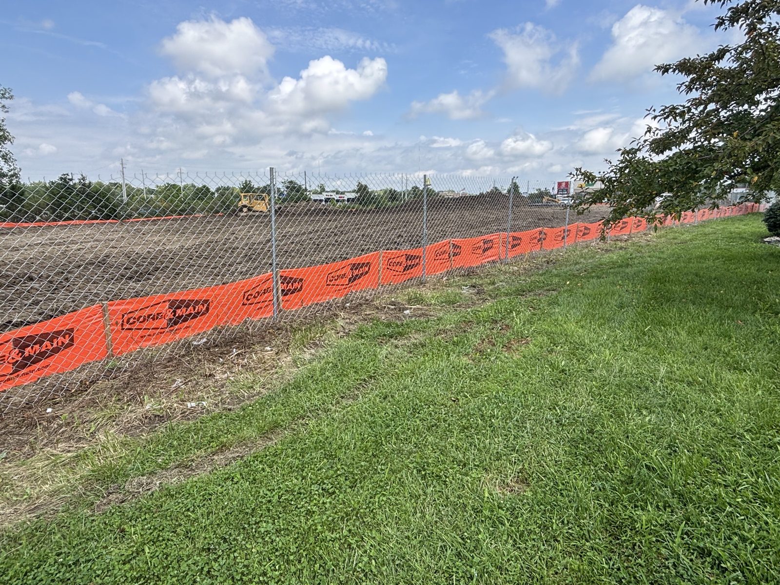 Chain link with orange safety mesh around a graded dirt lot