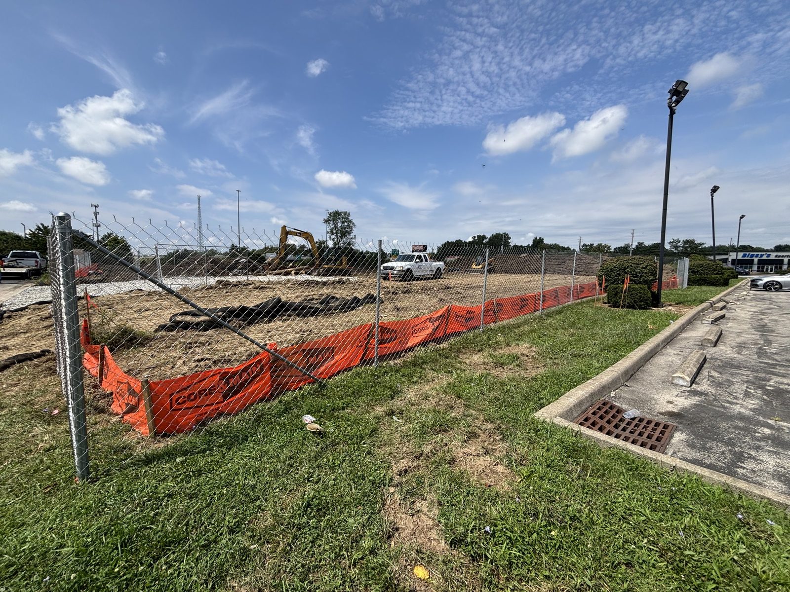 Chain link lined with orange safety fence around a graded site with an excavator