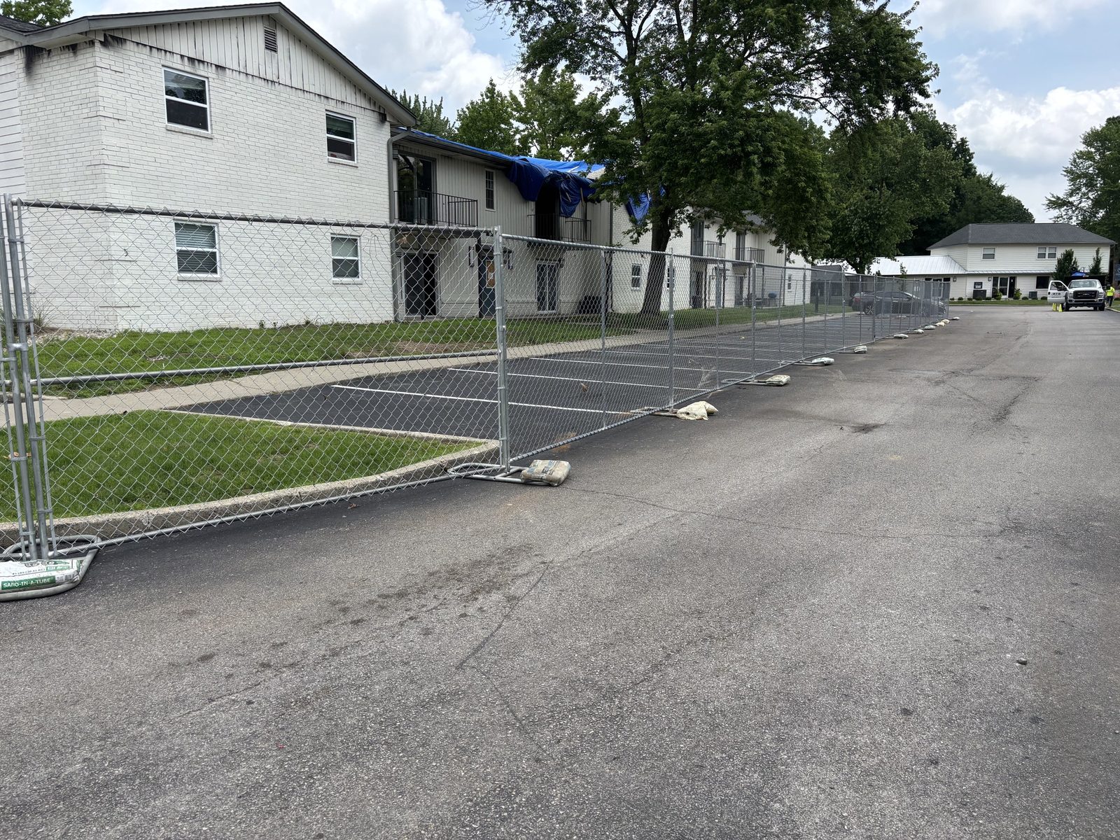 Panel fence on sandbagged stands along a parking lot beside a two-story apartment building