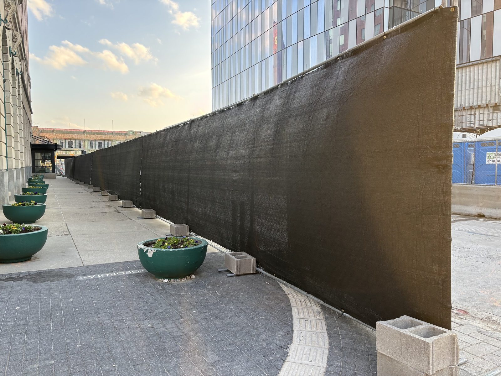 Black windscreen along a paved plaza lined with planters