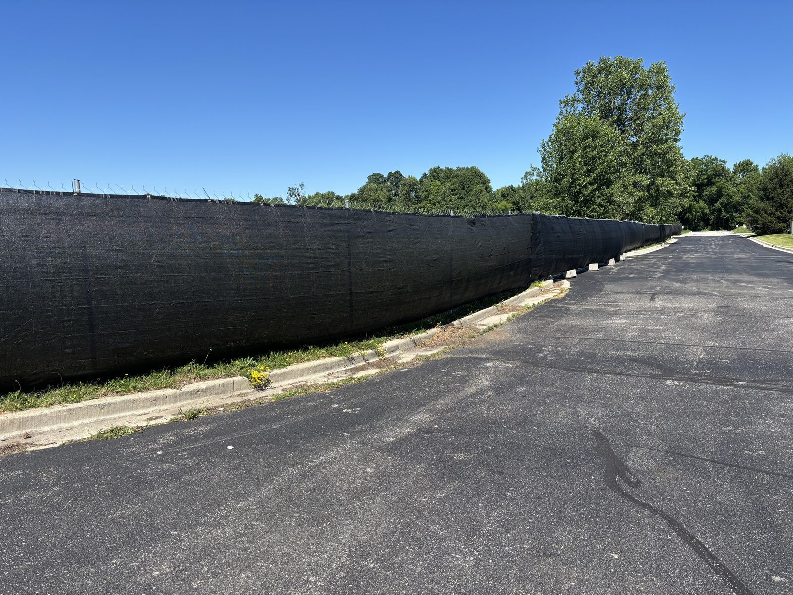 Long run of black windscreen on fence beside a paved drive