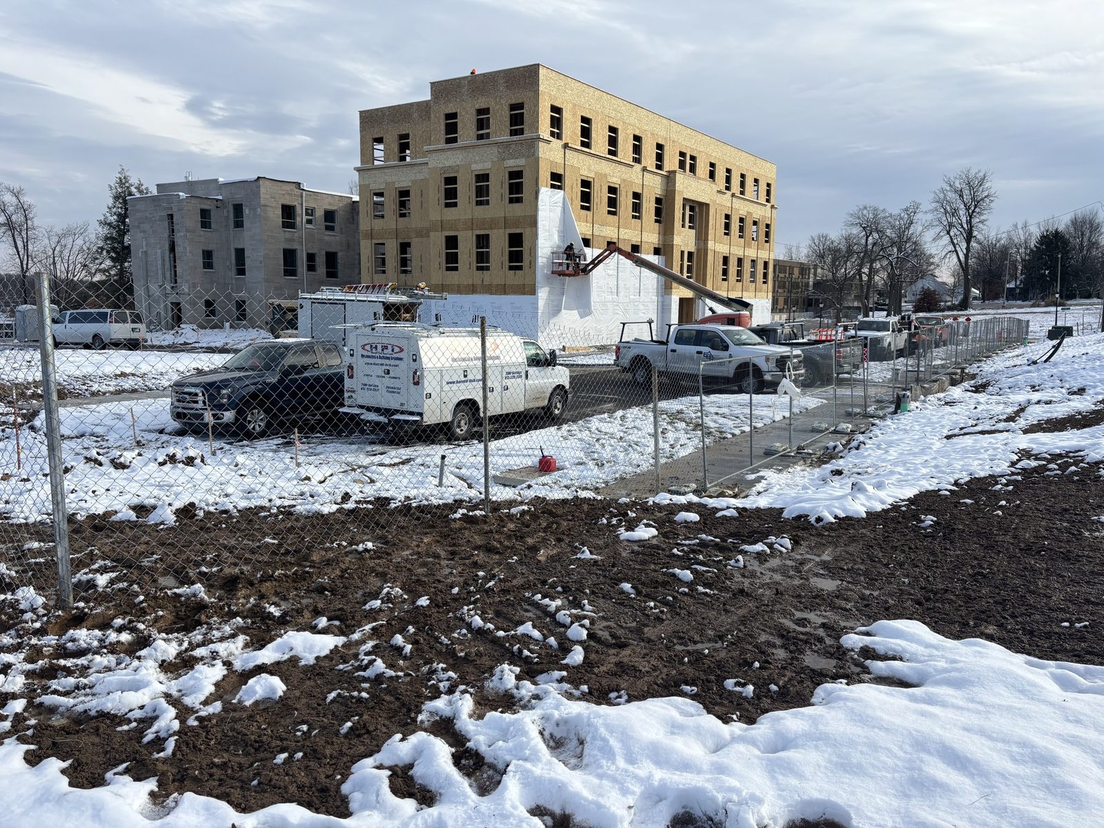 Chain link panels around a snowy construction site with a framed building